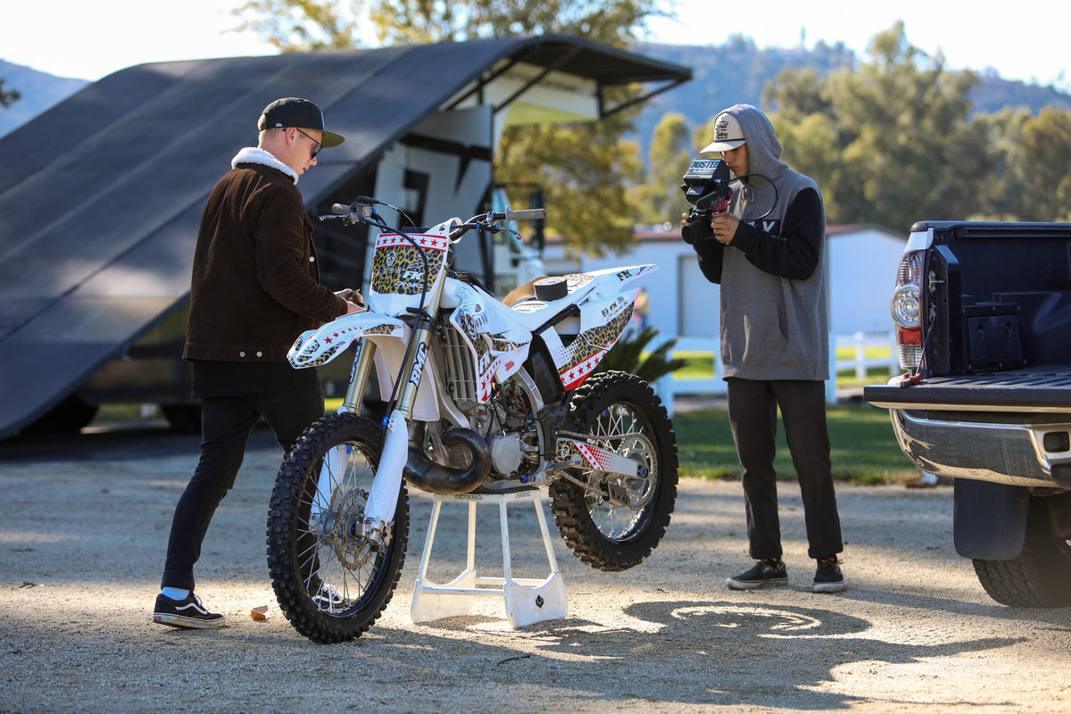 Pat Bowden working with a filmmaker beside his motorcycle and freestyle ramp.