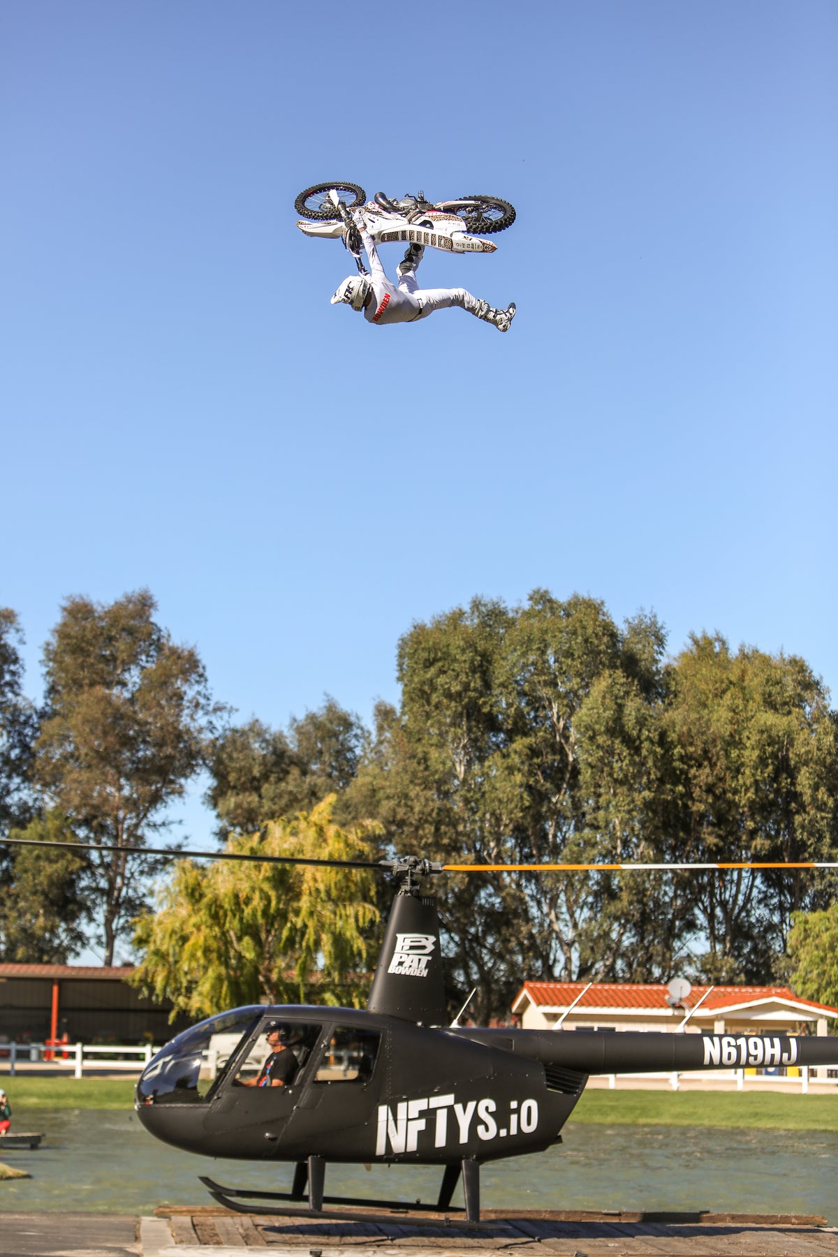 Pat Bowden performing a freestyle motocross trick above a helicopter