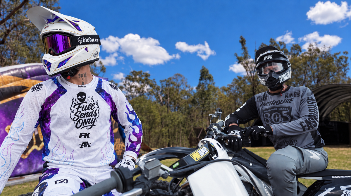 Two helmeted riders on motorbikes with an airbag and trees behind them